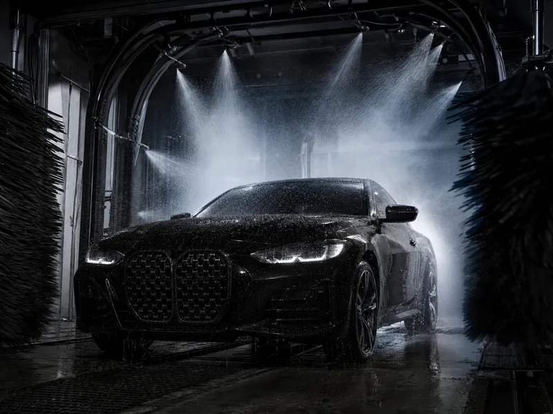 Black coupe passing through a backlit wash tunnel with fine water spray